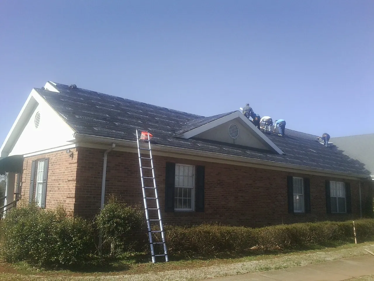 Crew tearing shingles off a brick ranch roof with a ladder set — Emergency Roof Repair work by our crew in Tamiment