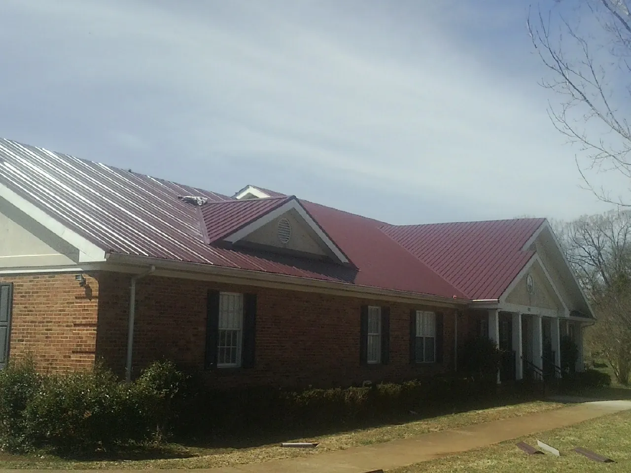 Red metal roof with gabled entries on a long brick building, from a Hail Damage Roof Repair job in Tamiment