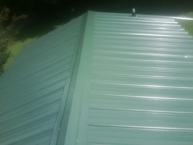 New green metal panels meeting at the ridge of a roof — Flat Roof Repair work by our crew in Tamiment
