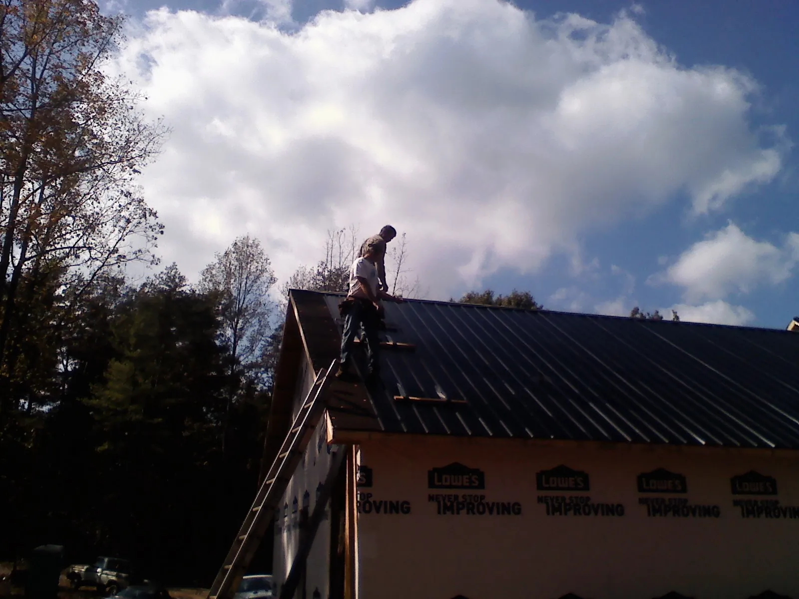 Roofer fastening dark metal panels high against a cloudy sky, from a Roof Inspection job in Tamiment