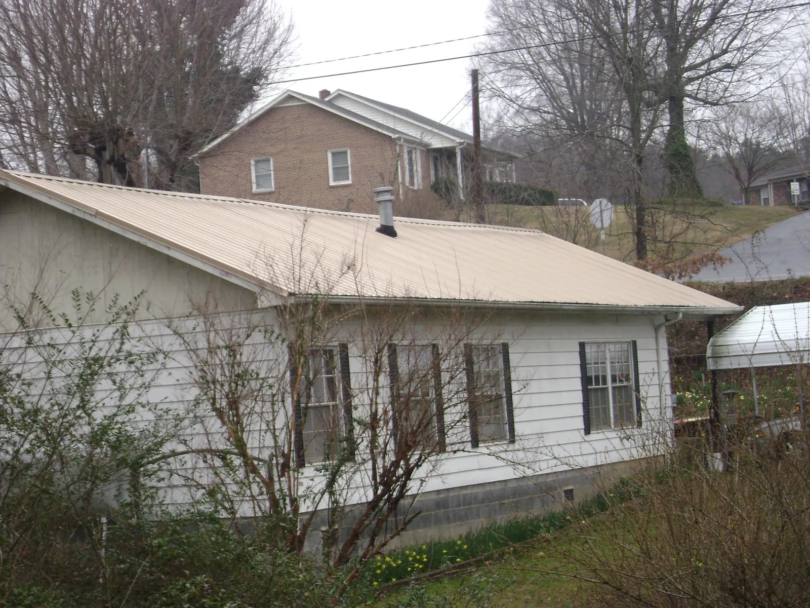 Tan metal roof on a white sided house set into a hillside — Commercial Roofing by Roofing Brothers in Tamiment